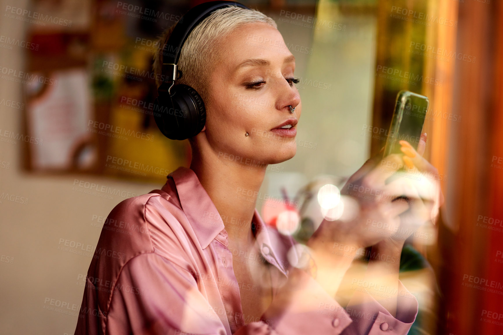Buy stock photo Shot of an attractive young woman listening to music and using her cellphone inside a local cafe