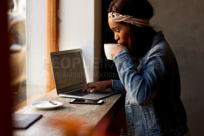 Buy stock photo Shot of an attractive young woman drinking coffee and using a laptop while relaxing inside a local cafe