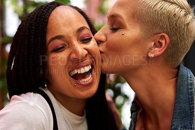 Buy stock photo Shot of an attractive young woman kissing her friend on the cheek while hanging out and having fun together outdoors