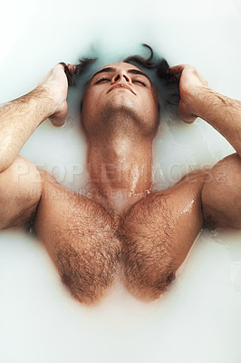 Buy stock photo High angle shot of a handsome young man lying in a bathtub full of milky water at home