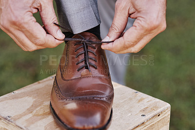 Buy stock photo Cropped shot of an unrecognizable mature bridegroom adjusting his shoelaces while preparing fir his wedding outdoors