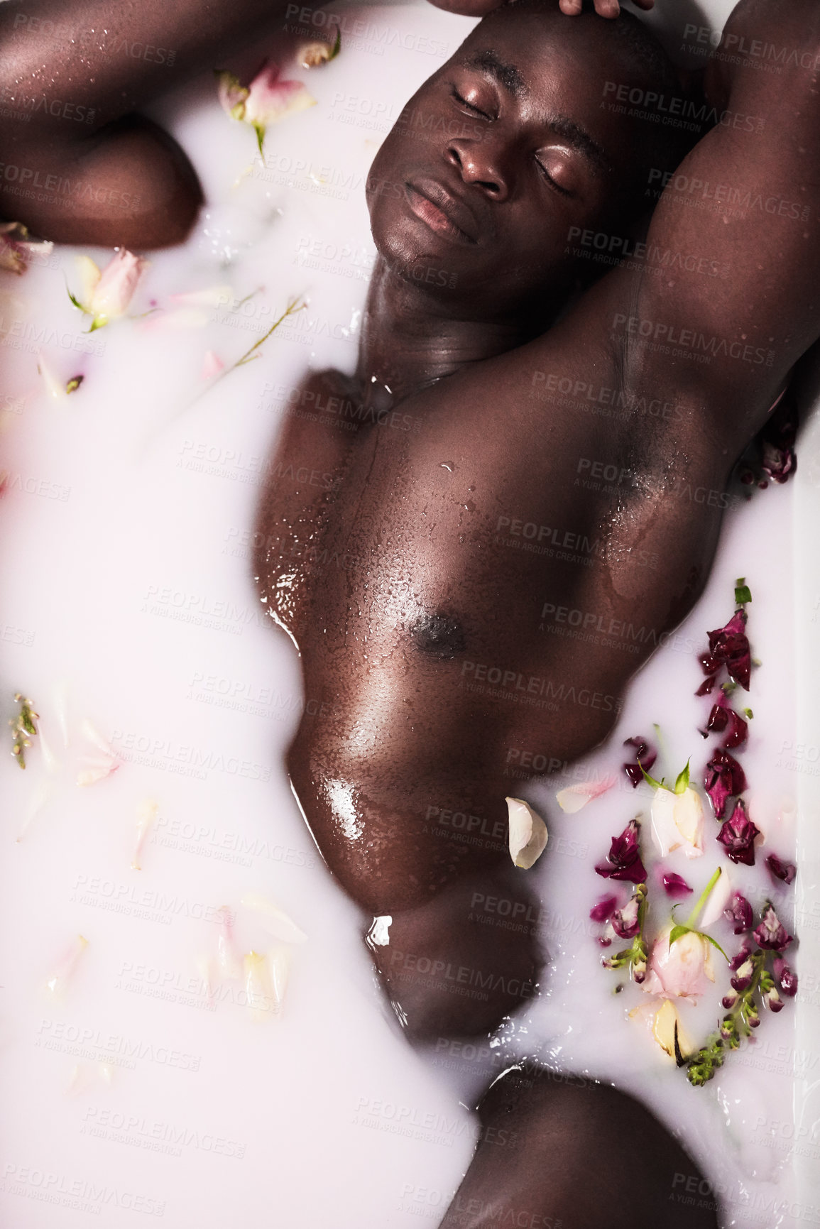 Buy stock photo Shot of a muscular young man having a milky bath filled with flowers at home