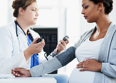 Buy stock photo Cropped shot of a confident female doctor checking the blood pressure of a pregnant patient at a hospital during the day