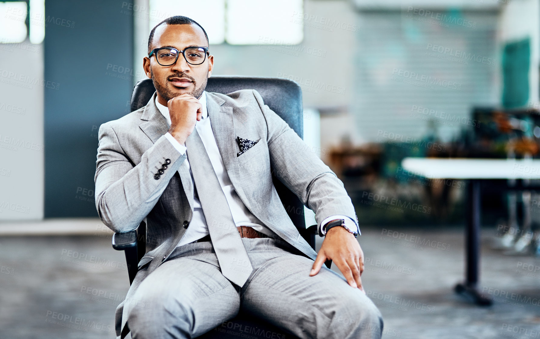 Buy stock photo Cropped portrait of a handsome young businessman sitting in his office and looking contemplative with his hand on his chin