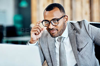 Buy stock photo Cropped shot of a handsome young businessman sitting alone in his office and smirking while using his laptop