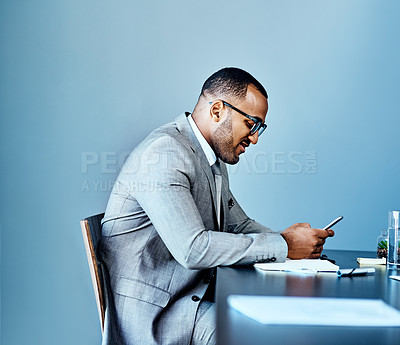 Buy stock photo Cropped shot of a handsome young businessman sitting alone in his office and using his cellphone