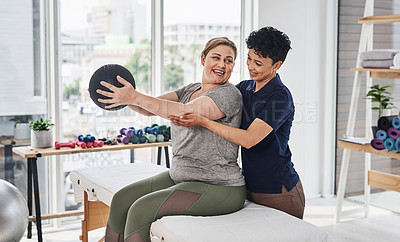 Buy stock photo Shot of a  young physiotherapist helping her mature patient exercise with a medicine ball inside her office at a clinic