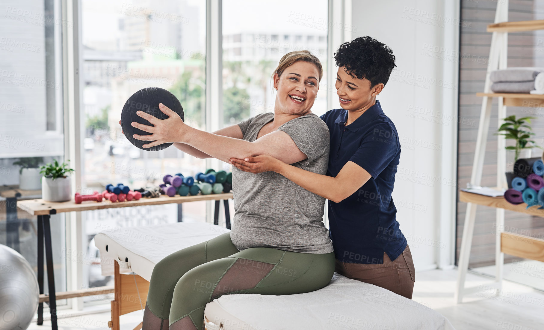 Buy stock photo Shot of a  young physiotherapist helping her mature patient exercise with a medicine ball inside her office at a clinic