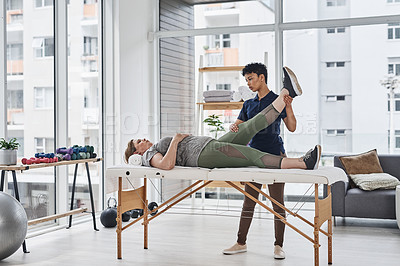Buy stock photo Full length shot of a young physiotherapist doing leg exercises with her patient inside her office at a clinic