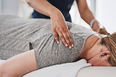 Buy stock photo Shot of a mature woman lying face down and getting her back massaged by a physiotherapist at a clinic