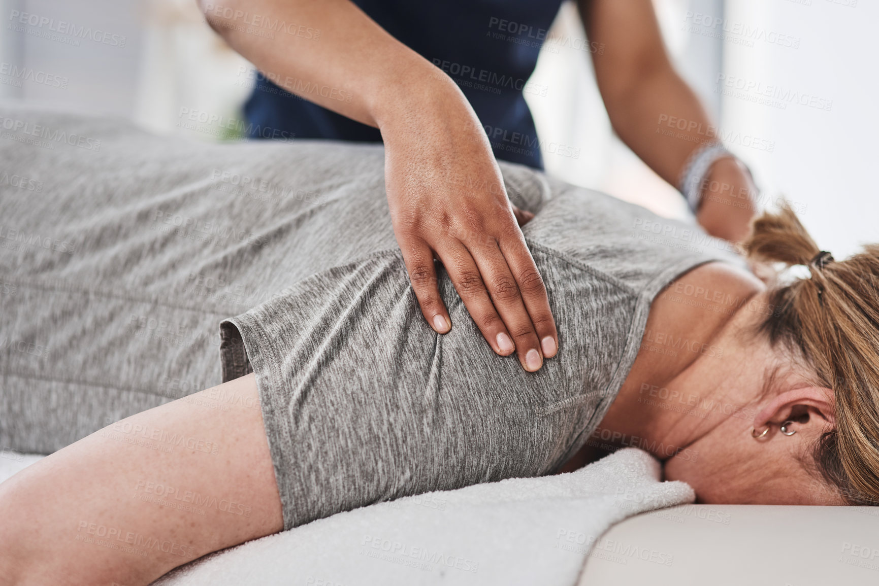 Buy stock photo Shot of a mature woman lying face down and getting her back massaged by a physiotherapist at a clinic
