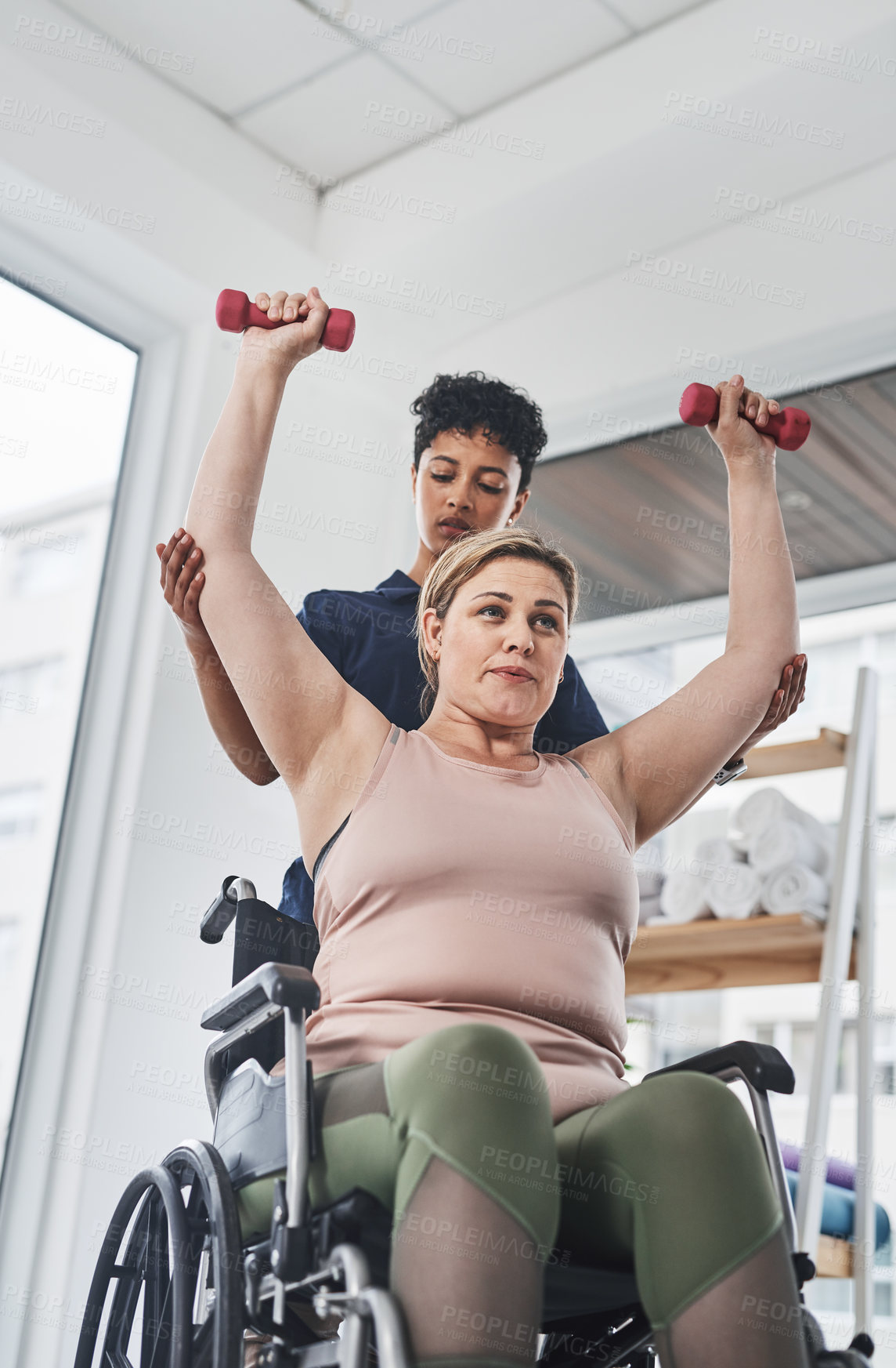 Buy stock photo Shot of a young physiotherapist helping her wheelchair bound patient exercise with dumbbells at a clinic