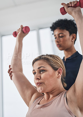 Buy stock photo Shot of a young physiotherapist helping her mature patient exercise with dumbbells at a clinic