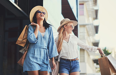 Buy stock photo Cropped shot of two attractive young girlfriends laughing while walking with shopping bags in the city during the day