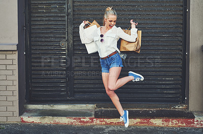 Buy stock photo Full length shot of an attractive young woman jumping for joy while holding shopping bags against an urban background