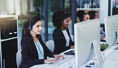 Buy stock photo Cropped shot of a diverse group of businesswomen wearing headsets and using computers while sitting in the office together