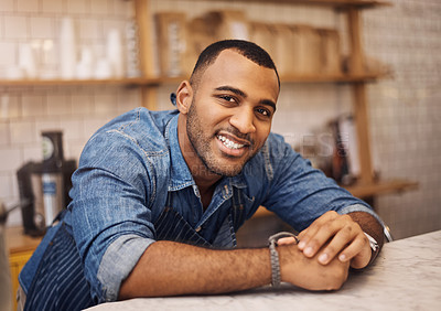 Buy stock photo Cropped shot of a handsome young businessman leaning on the counter in his cafe with his hands clasped