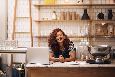 Buy stock photo Cropped shot of an attractive young businesswoman leaning on a counter in her cafe before working on her laptop