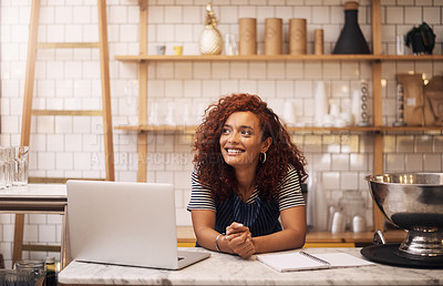 Buy stock photo Cropped shot of an attractive young businesswoman leaning on a counter in her cafe before working on her laptop