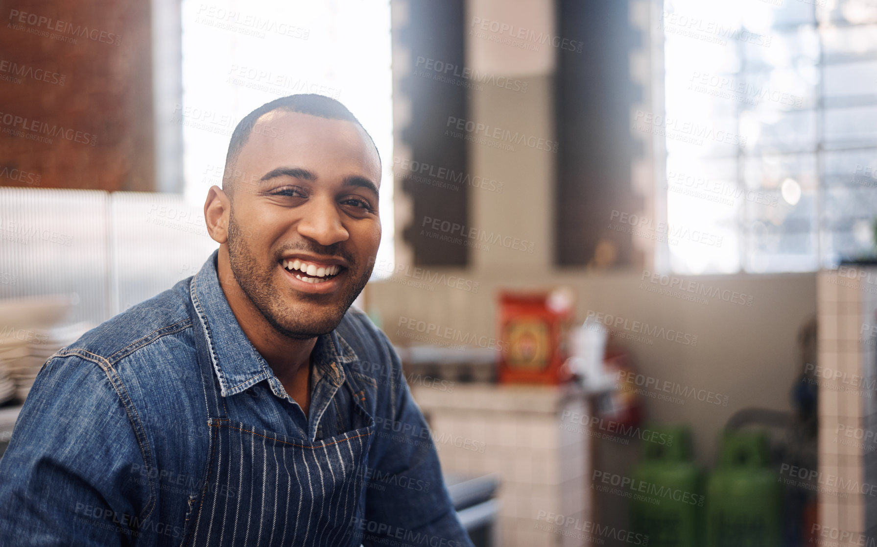 Buy stock photo Cropped shot a handsome young businessman standing alone in his cafe and smiling during the day