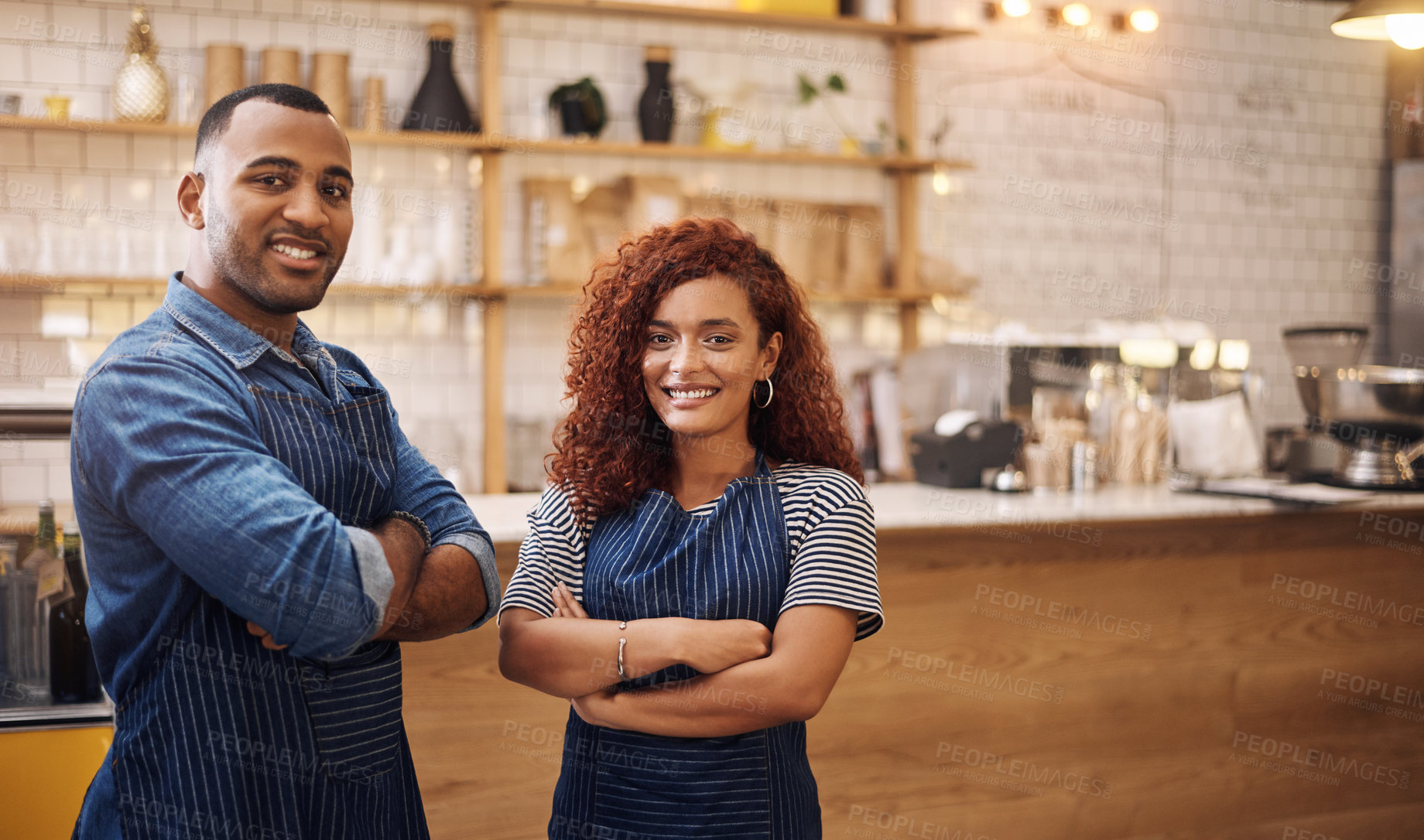 Buy stock photo Cropped shot of two young business owners standing in their cafe together with their arms folded