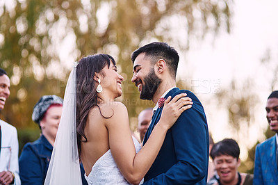 Buy stock photo Cropped shot of an affectionate young newlywed couple smiling at each other on their wedding day with their guests in the background