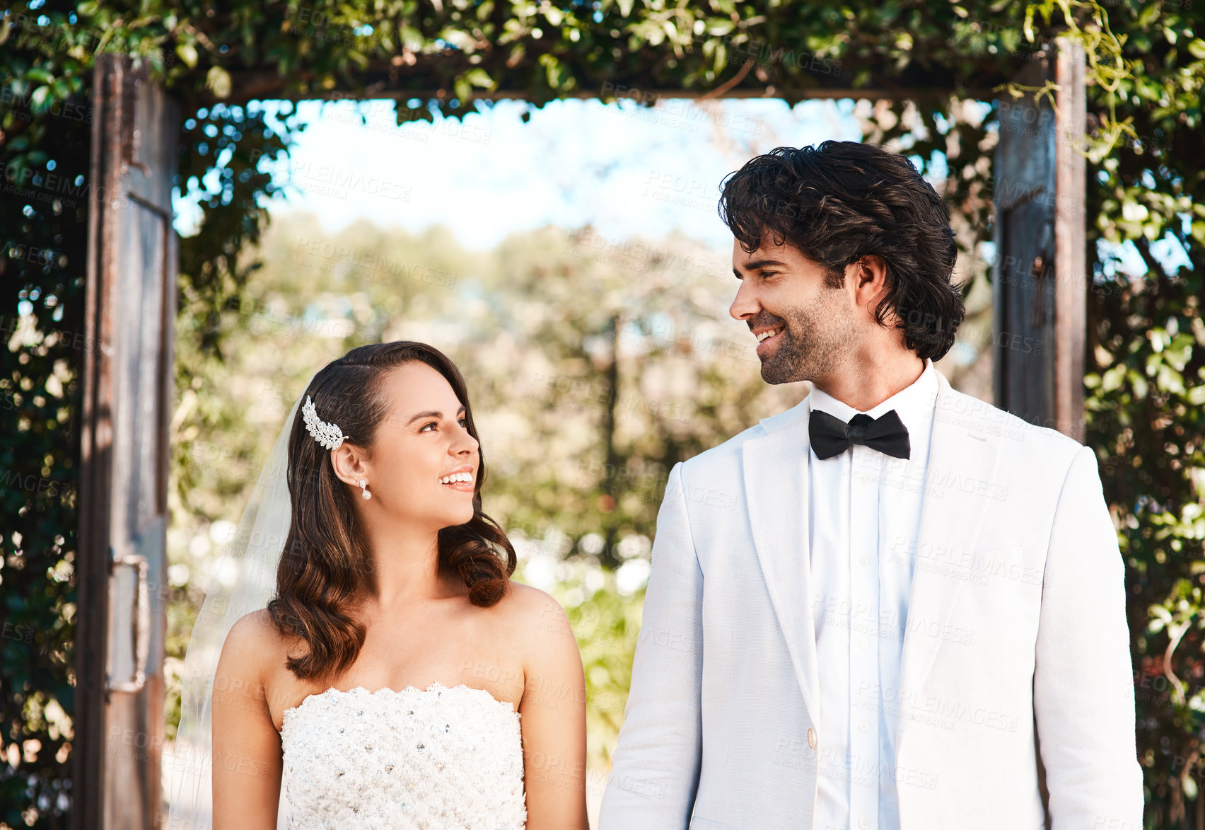 Buy stock photo Cropped shot of an affectionate young newlywed couple smiling at each other while standing outdoors on their wedding day