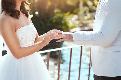 Buy stock photo Cropped shot of an unrecognizable bride slipping a ring on to her groom's finger while standing outdoors on their wedding day