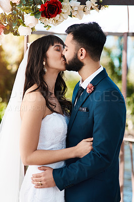 Buy stock photo Cropped shot of an affectionate young newlywed couple kissing while standing outdoors on their wedding day