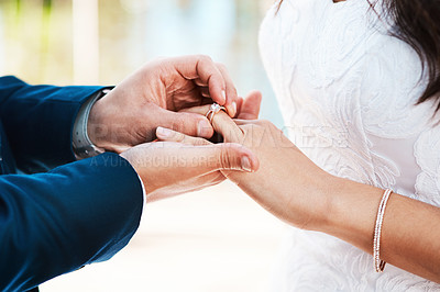 Buy stock photo Cropped shot of an unrecognizable groom slipping a ring on to his bride's finger while standing outdoors on their wedding day
