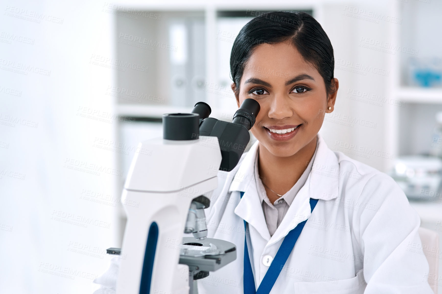 Buy stock photo Cropped portrait of an attractive young female scientist smiling while working with a microscope in a laboratory