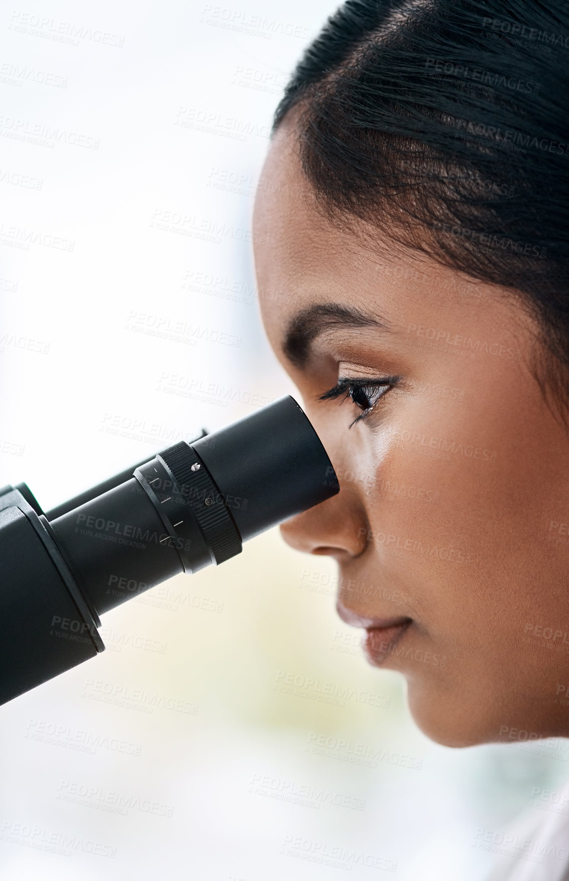 Buy stock photo Closeup shot of an attractive young female scientist looking through a microscope while working in a laboratory