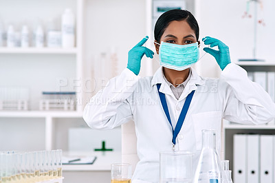 Buy stock photo Cropped shot of an attractive young female scientist putting on a mask while working in a laboratory