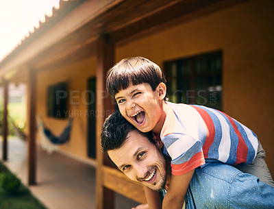 Buy stock photo Cropped portrait of an affectionate young father piggybacking his little son while standing in their backyard at home