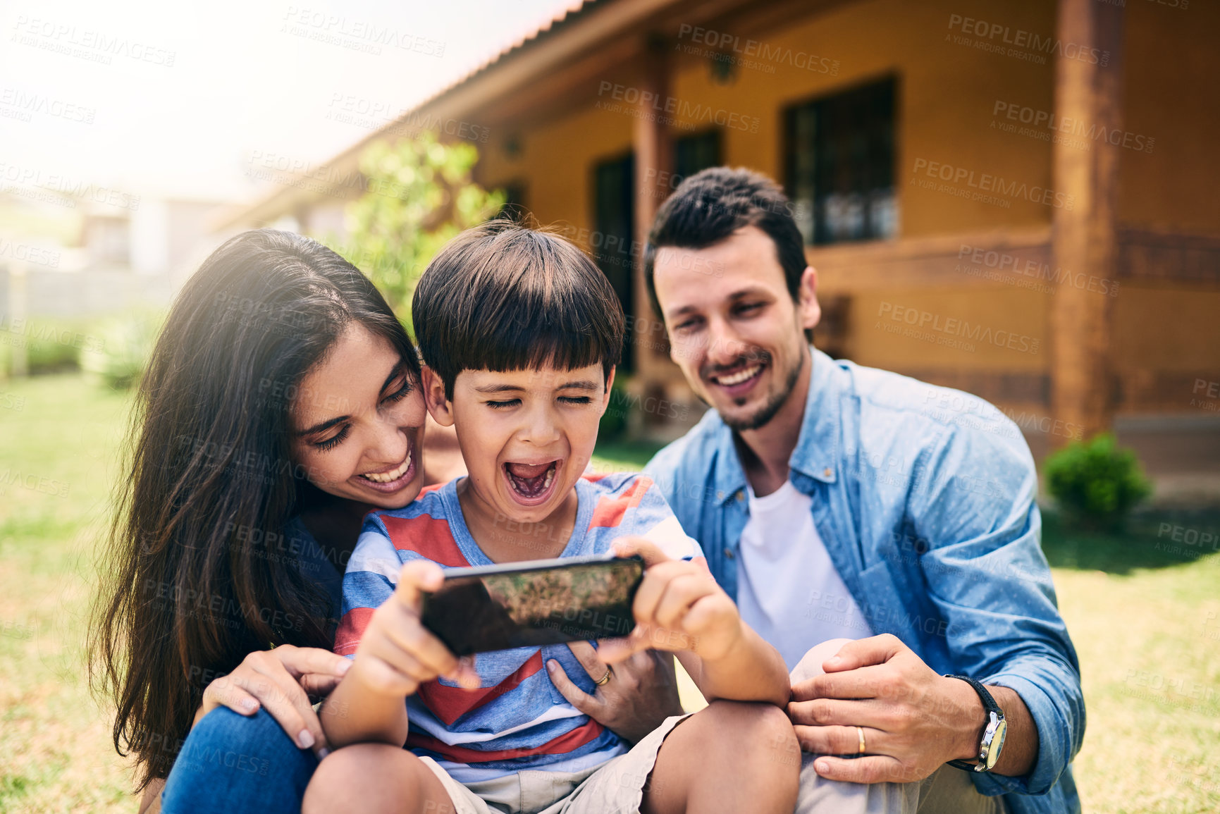 Buy stock photo Cropped shot of an affectionate young family of three taking a selfie together while sitting on the loan in their backyard at home