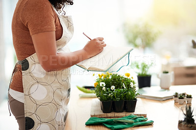Buy stock photo Cropped shot of an unrecognizable young female botanist making notes while working in her florist