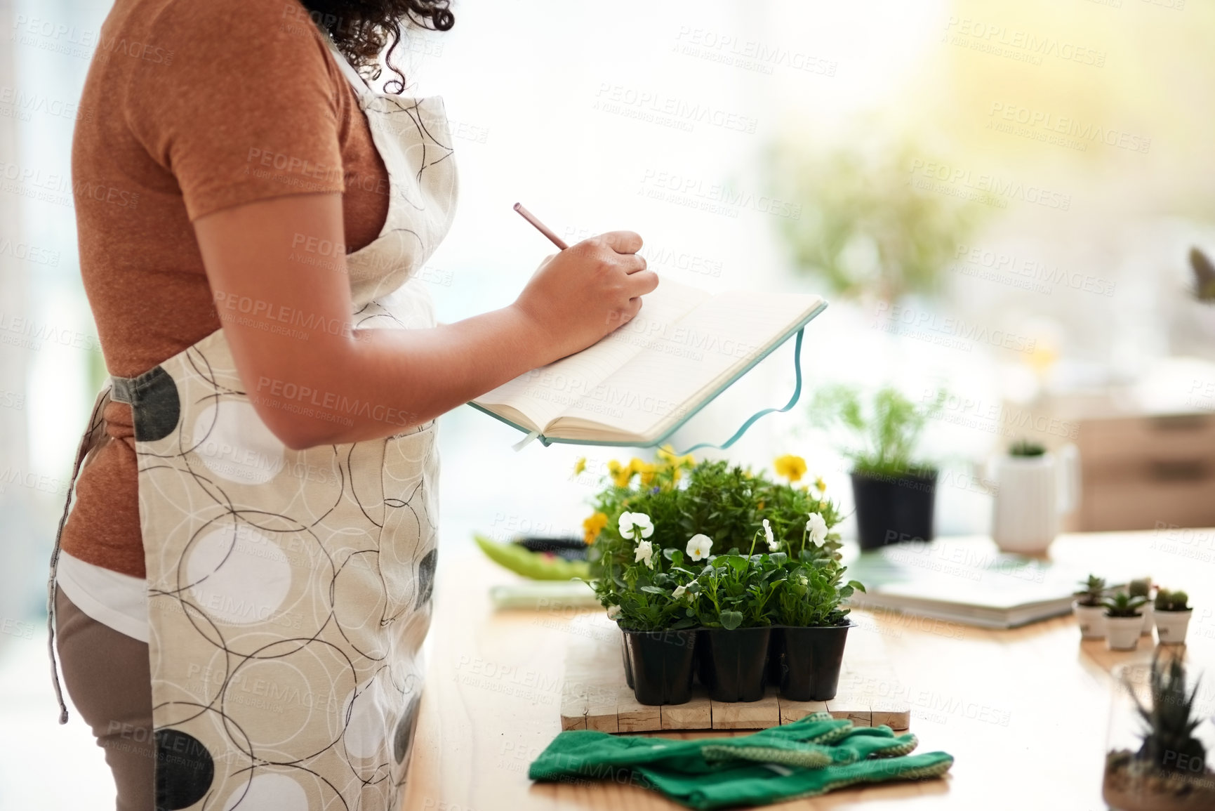 Buy stock photo Cropped shot of an unrecognizable young female botanist making notes while working in her florist