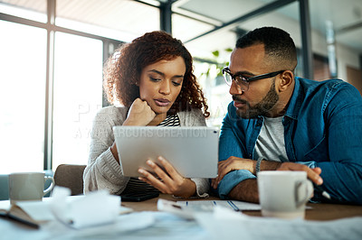 Buy stock photo Shot of a young couple using a digital tablet while planning their budget together at home
