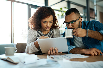 Buy stock photo Shot of a young couple using a digital tablet while planning their budget together at home