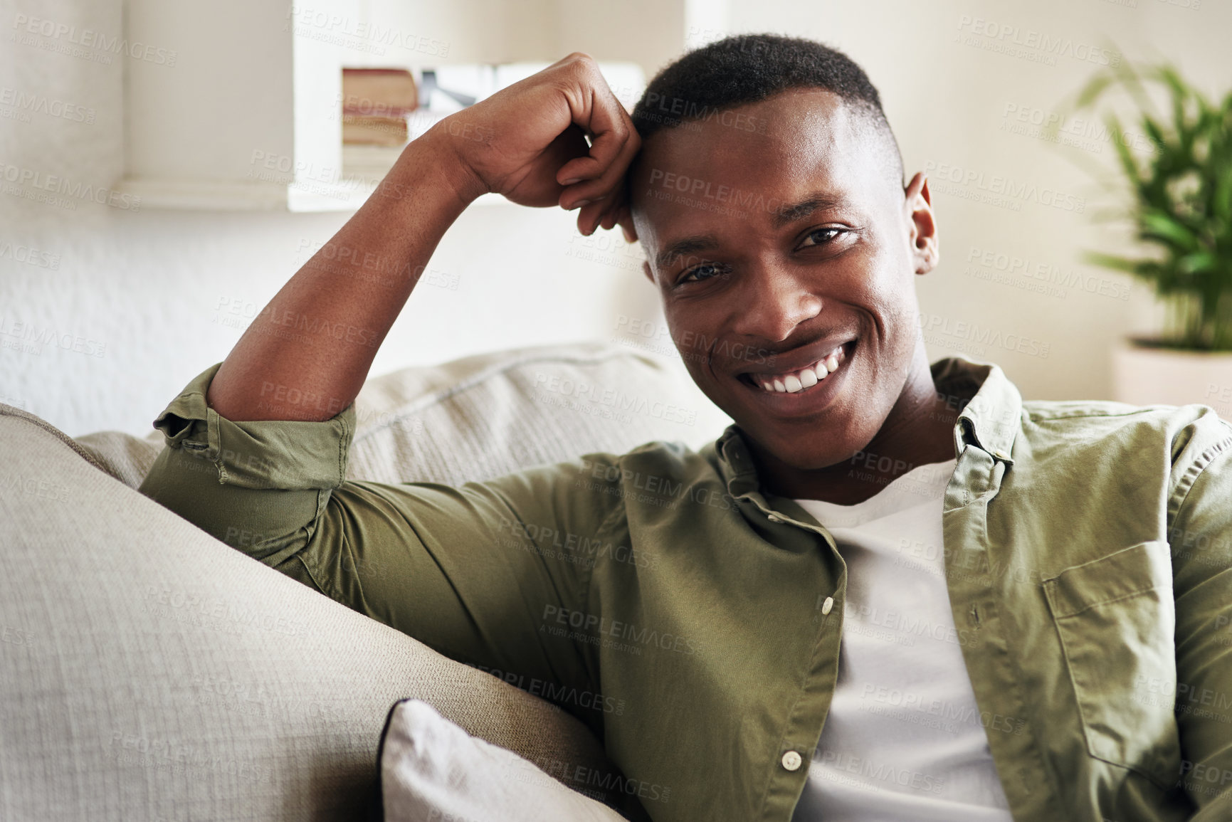 Buy stock photo Cropped portrait of a handsome young man smiling while relaxing on his couch at home