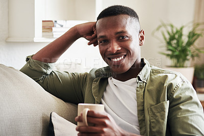 Buy stock photo Cropped portrait of a handsome young man smiling while having coffee on his couch at home