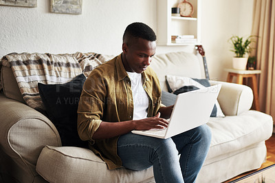 Buy stock photo Cropped shot of a handsome young man using a laptop while relaxing on his couch at home