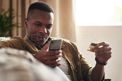 Buy stock photo Cropped shot of a handsome young man using a smartphone and a credit card to shop online while sitting on his couch at home