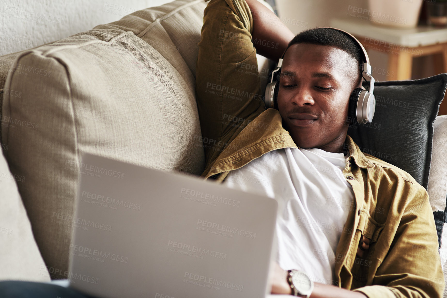 Buy stock photo Cropped shot of a handsome young man using a laptop while listening to music on his headphones in his living room at home