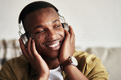 Buy stock photo Cropped shot of a handsome young man smiling while listening to music on his headphones in his living room at home