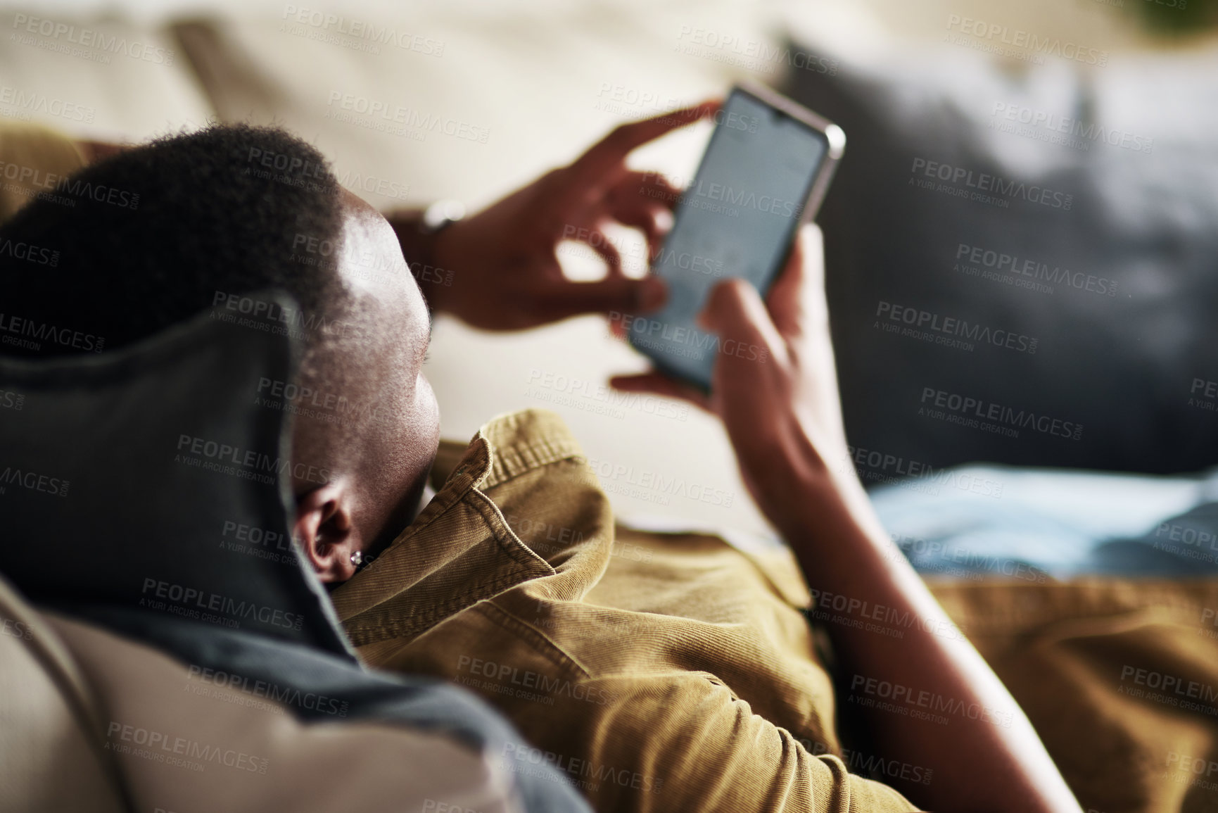 Buy stock photo Cropped shot of an unrecognizable man using a smartphone while relaxing on his couch at home