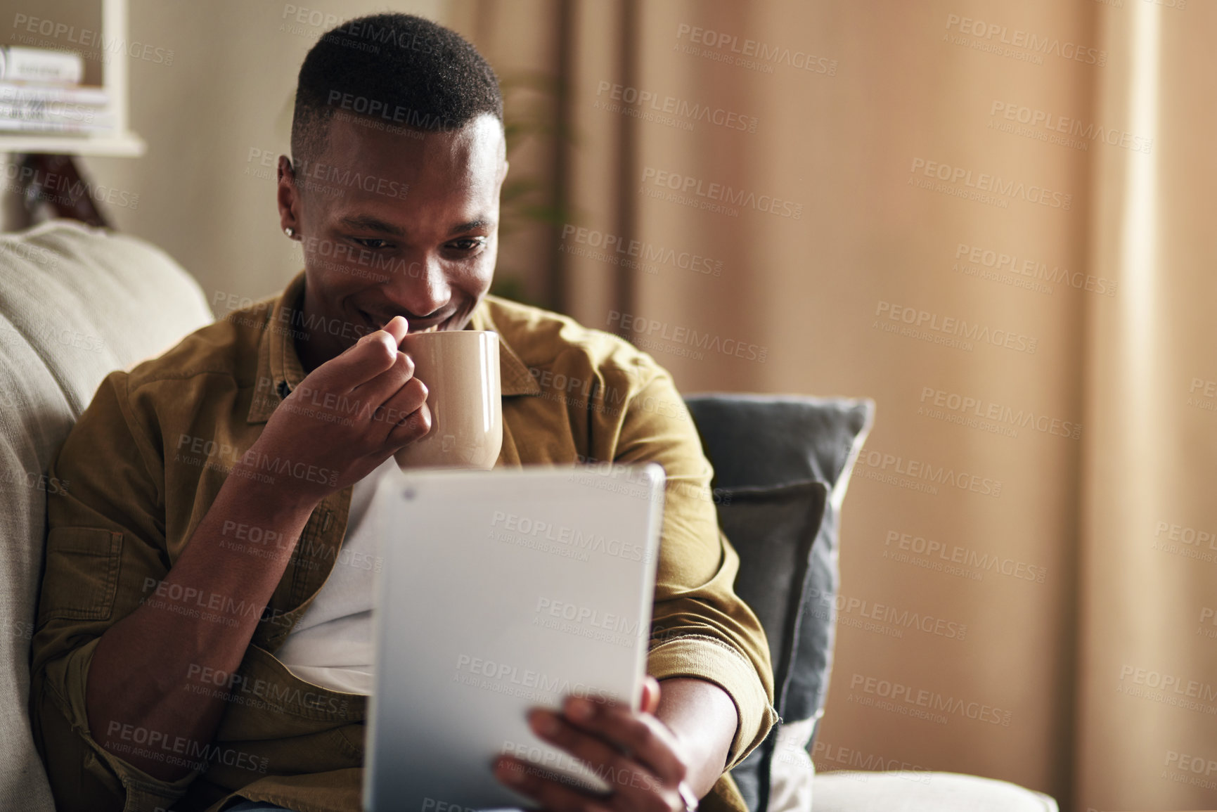 Buy stock photo Cropped shot of a handsome young man drinking coffee while using a digital tablet in his living room at home