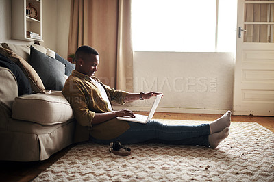 Buy stock photo Full length shot of a handsome young man using a laptop while sitting on the floor in his living room at home