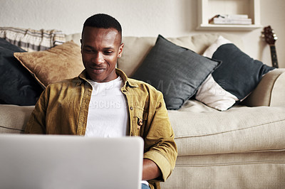 Buy stock photo Cropped shot of a handsome young man using a laptop while sitting on the floor in his living room at home