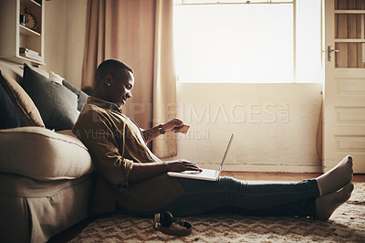 Buy stock photo Full length shot of a handsome young man using a laptop and a credit card to shop online while sitting on the floor in his living room at home